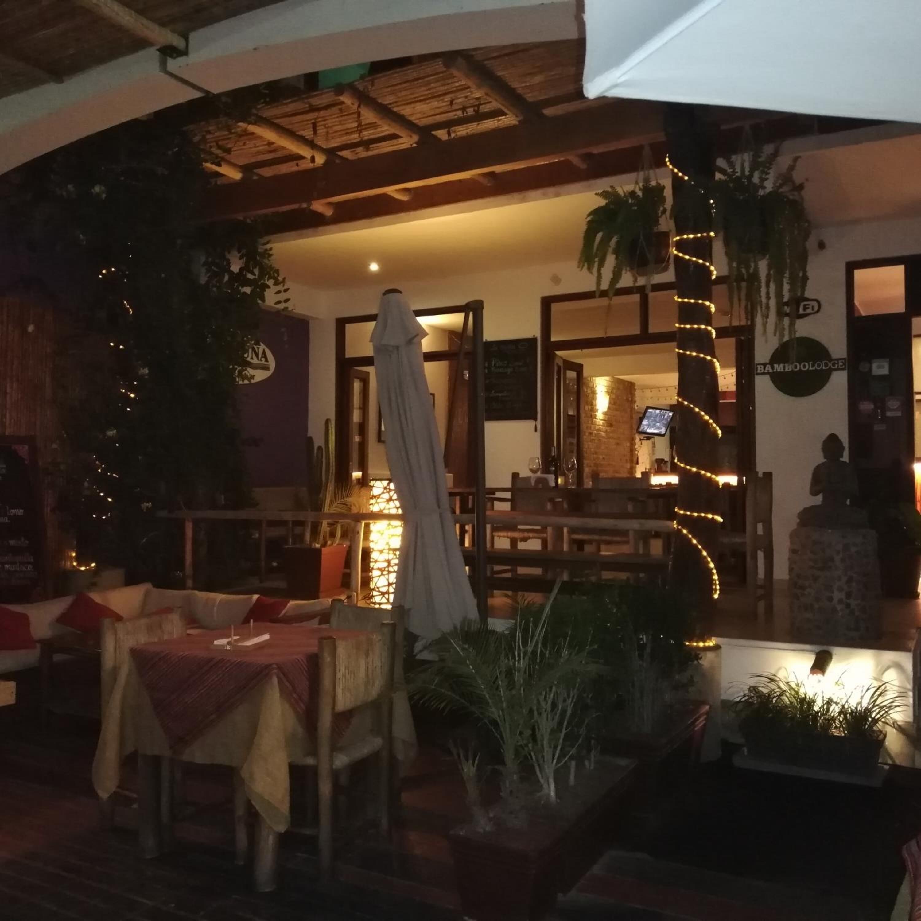 An outdoor dining area with tables and chairs, a covered seating area, and a sign for 'Bamboo Lodge'.