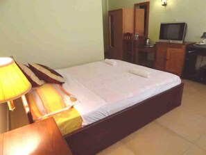 A single bed with a wooden frame, a bedside table with a lamp, a television on a stand, and a wardrobe in a room with plain walls. - Green Park Village Guesthouse (Siem Reap)