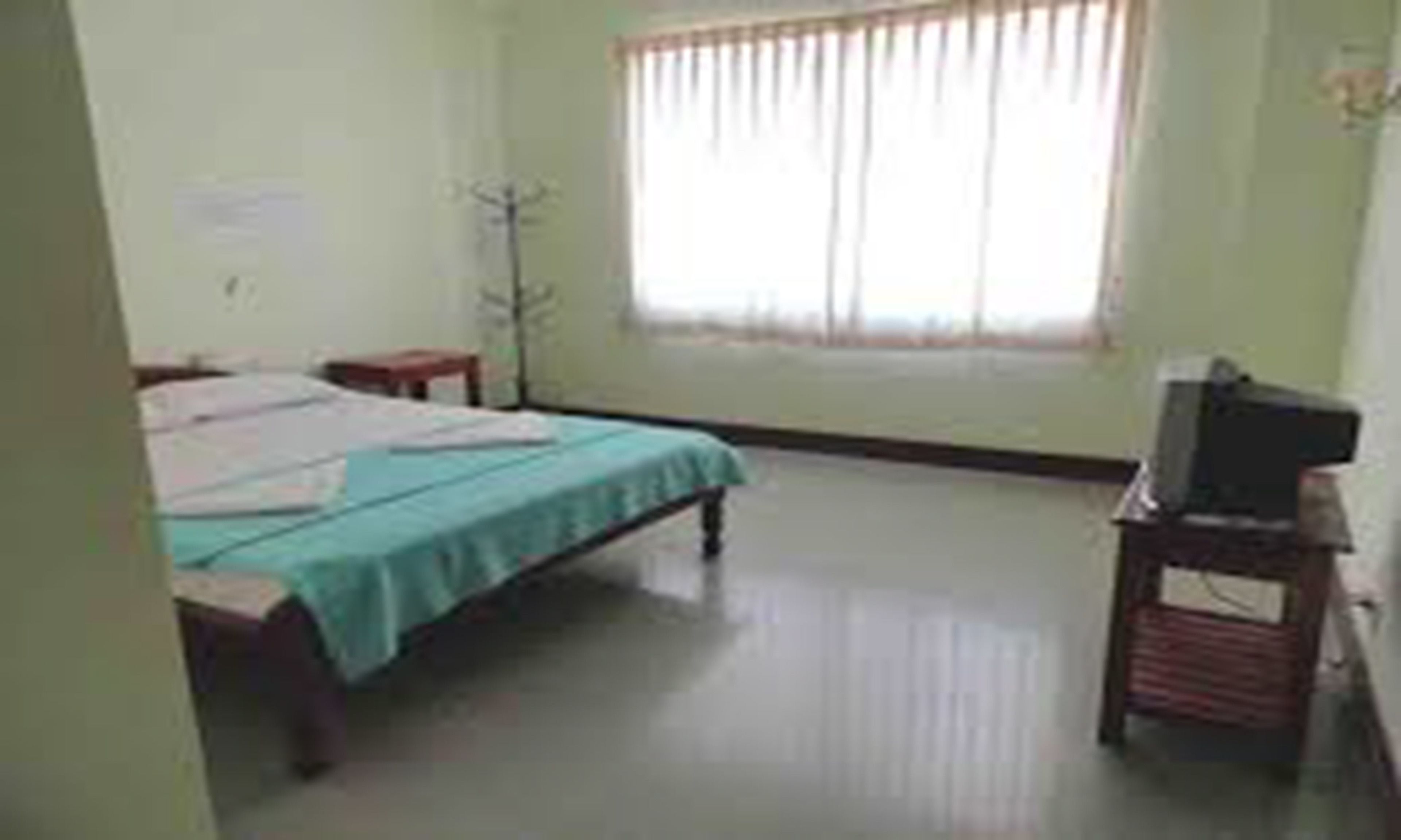 Una habitación con cama, escritorio, silla, televisor y ventana con cortinas.