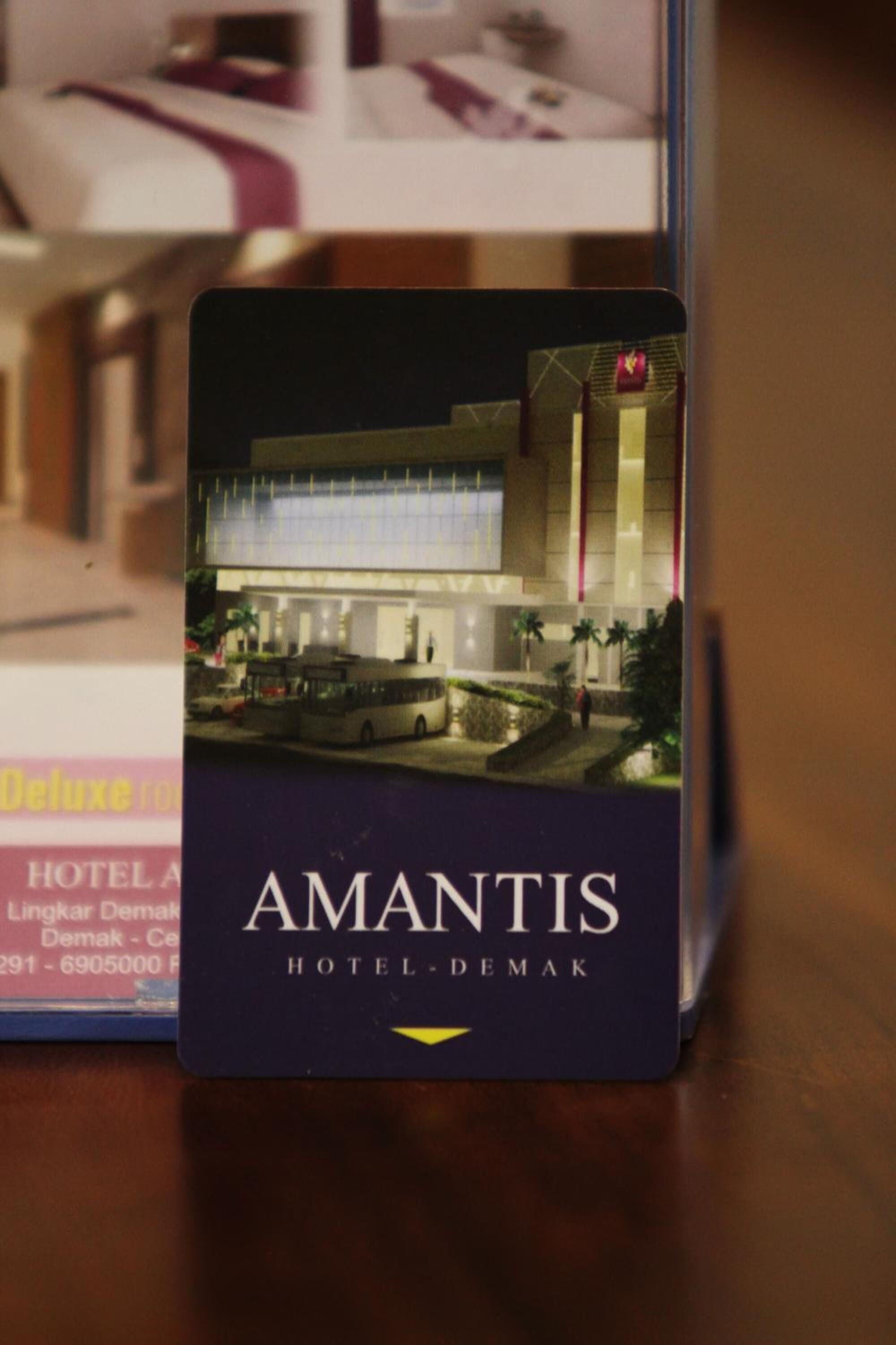 A hotel card for Amantis Hotel-Demak, featuring a modern building facade with a prominent entrance and a parking area.
