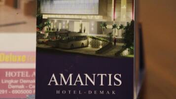 A hotel card for Amantis Hotel-Demak, featuring a modern building facade with a prominent entrance and a parking area.