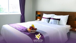 A hotel room with a neatly made bed, a fruit basket on the bed, and a window with curtains. - Amantis Hotel (Demak)