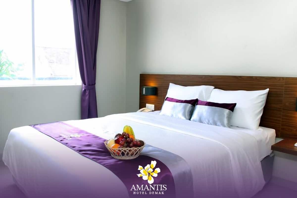 Quarto de hotel com cama bem arrumada, uma cesta de frutas sobre a cama e uma janela com cortinas.