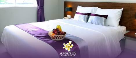 Una habitación de hotel con una cama bien hecha, una cesta de frutas sobre la cama y una ventana con cortinas.