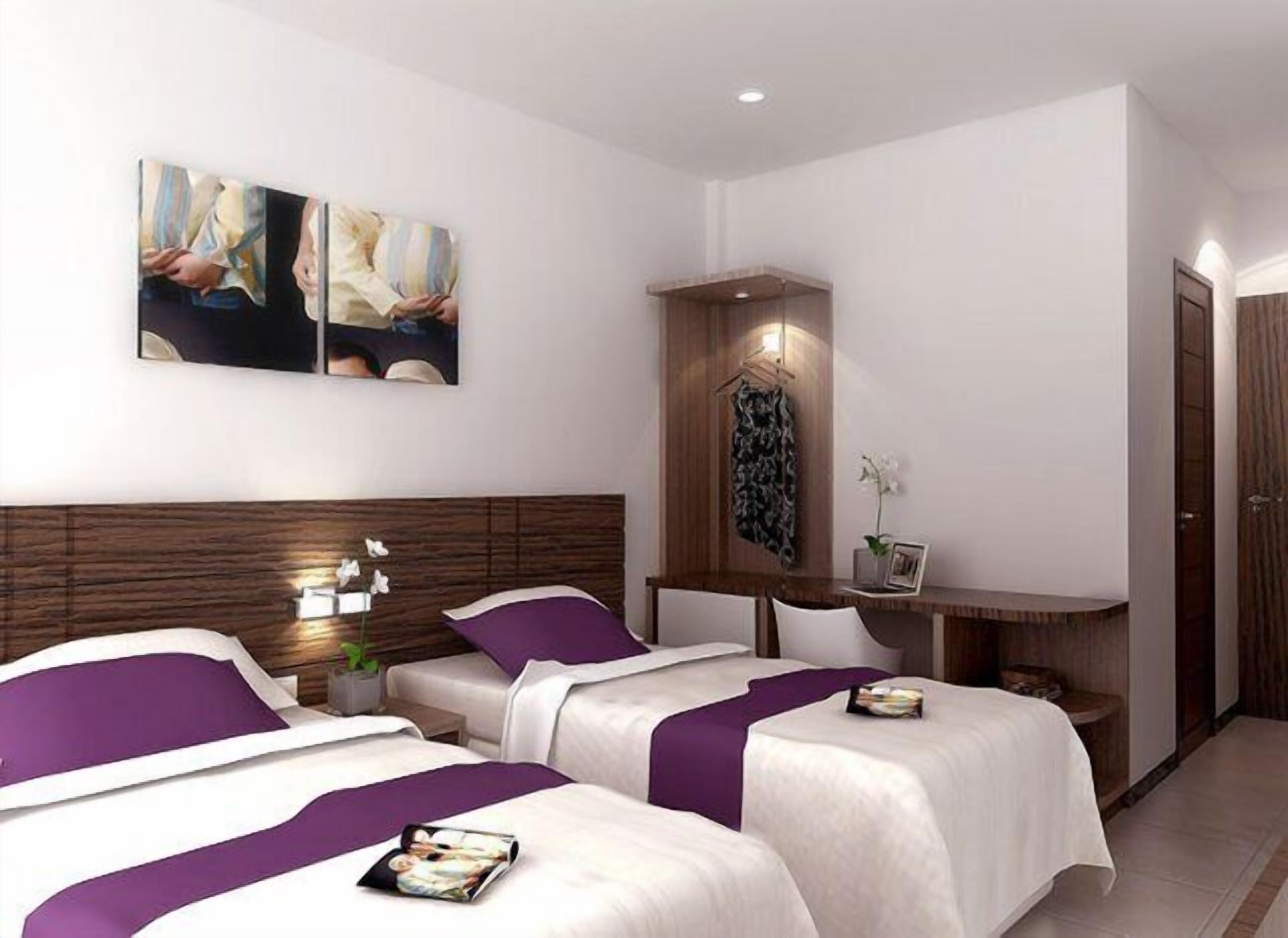 A hotel room with two beds, a wooden headboard, a desk with a chair, and a small table with a plant.