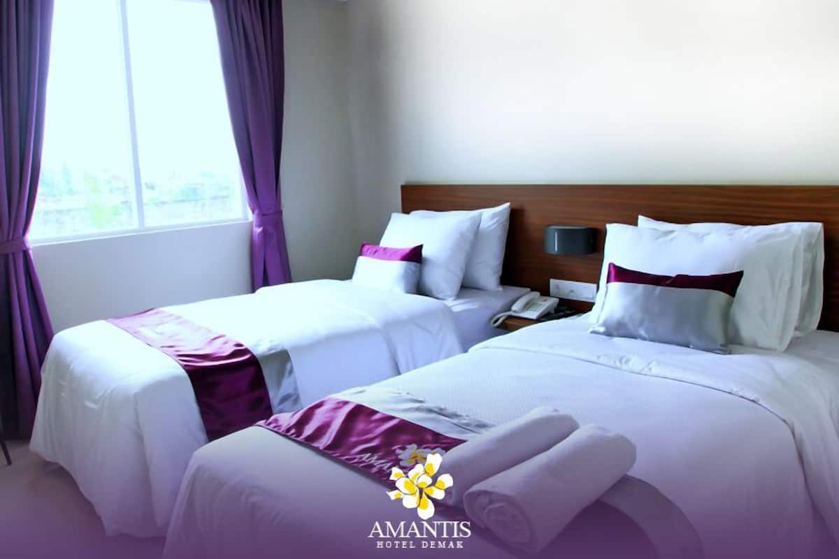Quarto de hotel com duas camas, mesa de cabeceira, telefone e janela com cortinas.