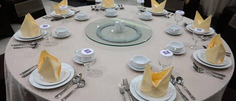 Una mesa redonda dispuesta con platos blancos, servilletas dobladas y cubiertos.