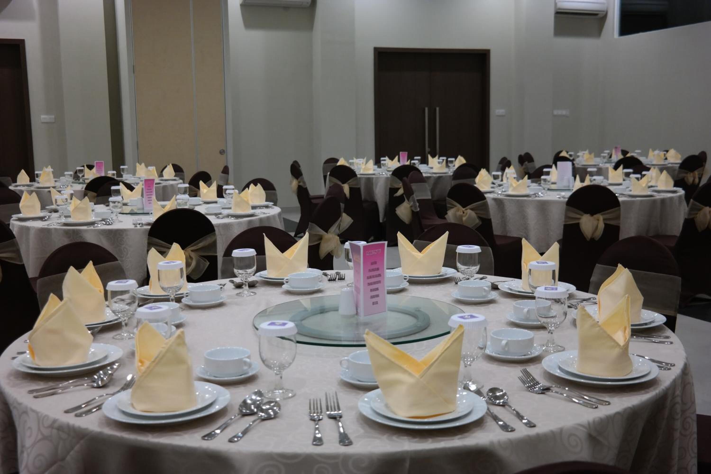 A banquet hall with round tables set for a formal event, each with folded napkins, cutlery, and glassware.