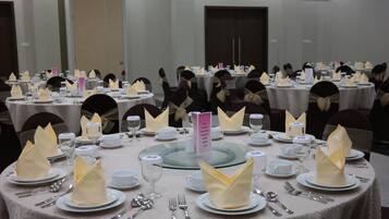 Un salón de banquetes con mesas redondas dispuestas para un evento formal, cada una con servilletas dobladas, cubiertos y cristalería.