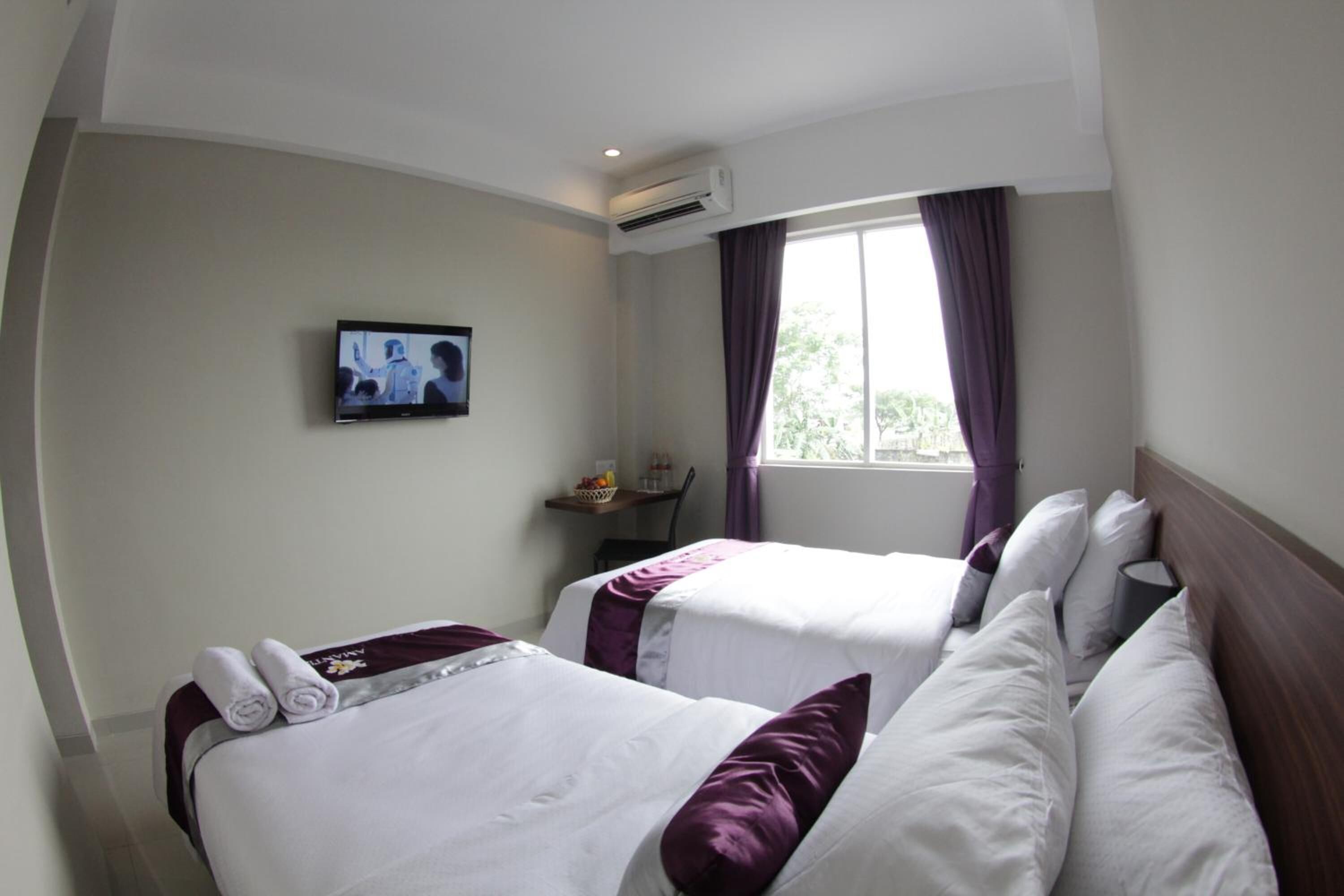 Habitación de hotel con dos camas, un televisor en la pared, un aire acondicionado y una ventana con cortinas.