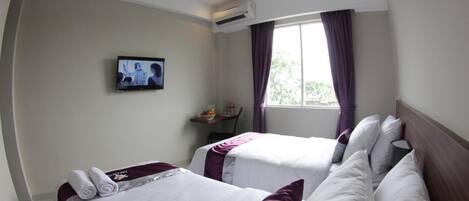 Habitación de hotel con dos camas, un televisor en la pared, un aire acondicionado y una ventana con cortinas.