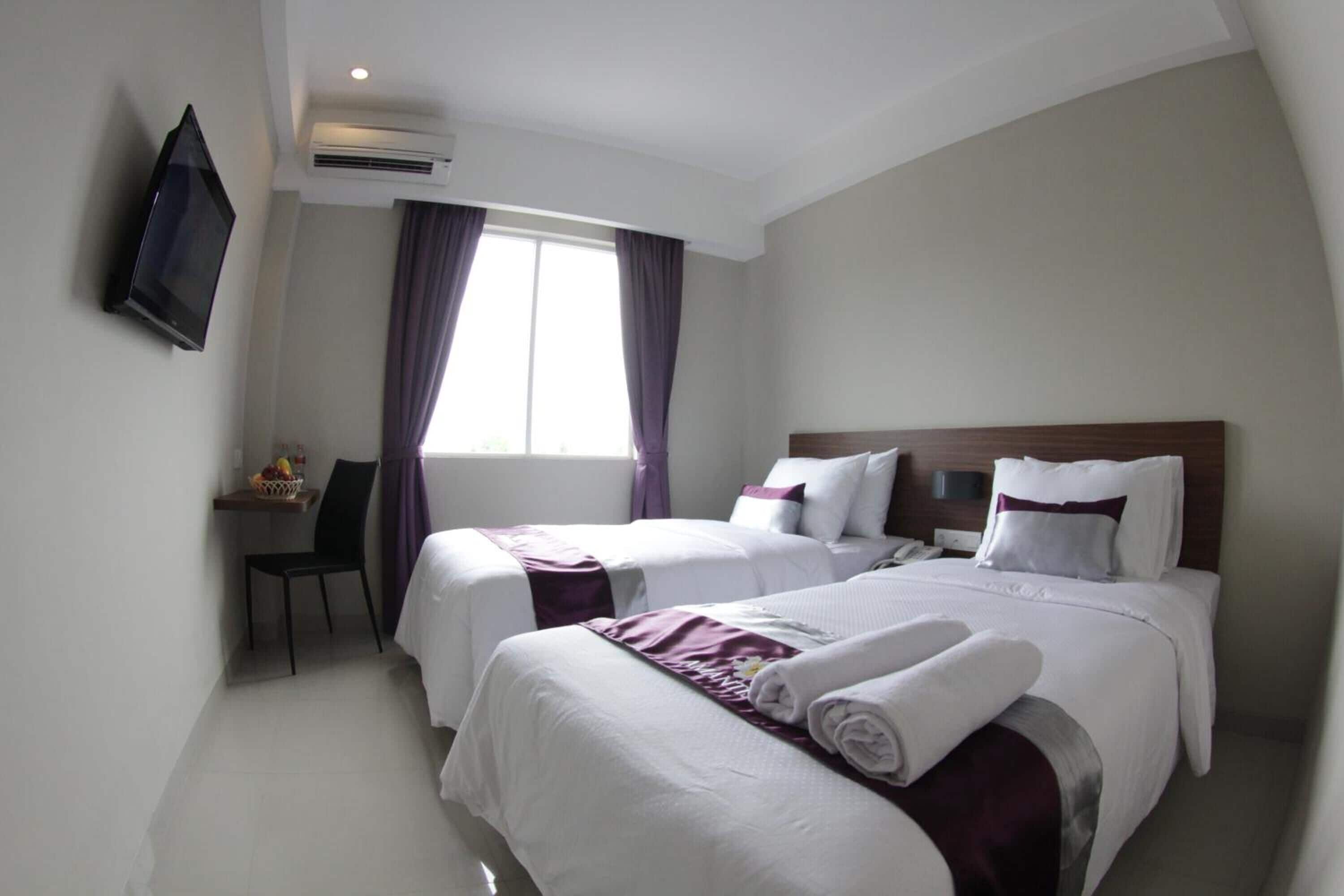 A hotel room with two beds, a desk, and a TV.