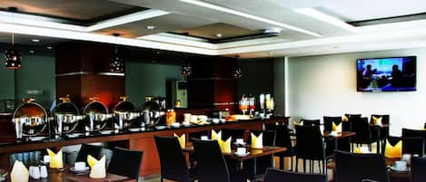 A modern hotel dining area with a long counter, multiple tables, and chairs.