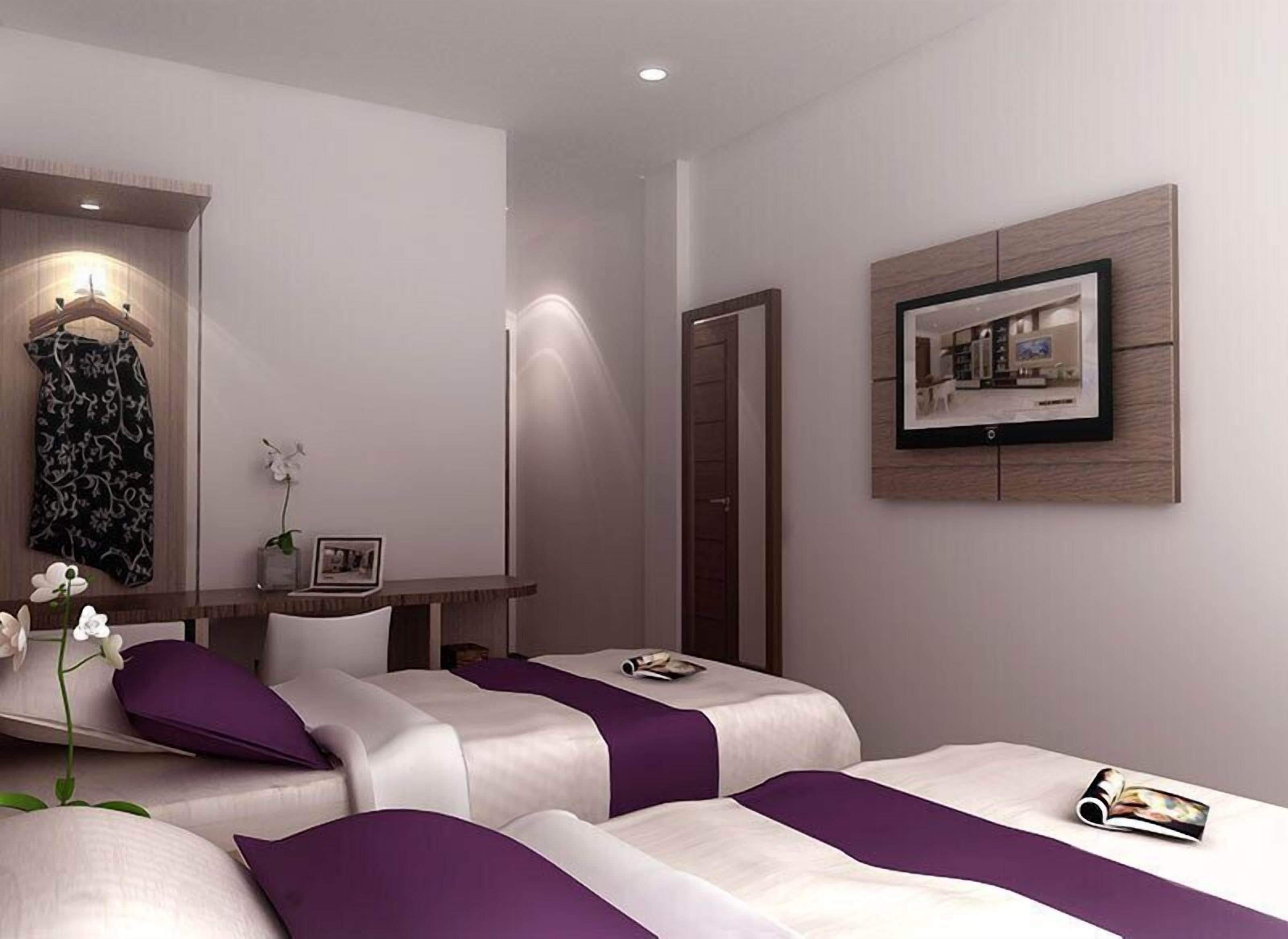 A modern hotel room with two beds, a desk, a chair, a wardrobe, and a framed picture on the wall.