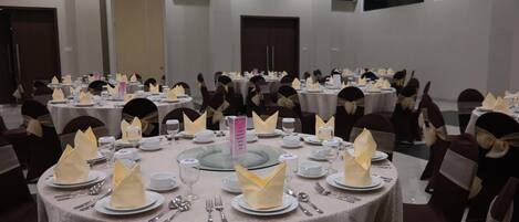 A banquet hall with round tables set for a formal event, featuring neatly folded napkins, plates, and cutlery.