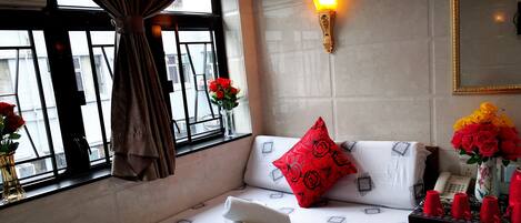 Habitación de hotel con cama, ventana con cortinas, luz en la pared y un jarrón con flores.