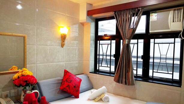 A hotel room with a bed, a bedside table with a vase of flowers, a lamp, and a window with curtains. - Germany Hostel (Kowloon)