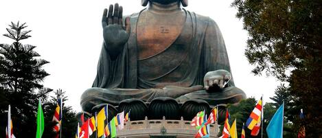 Une grande statue de Bouddha, le bras levé, entourée d’un escalier et de divers drapeaux.