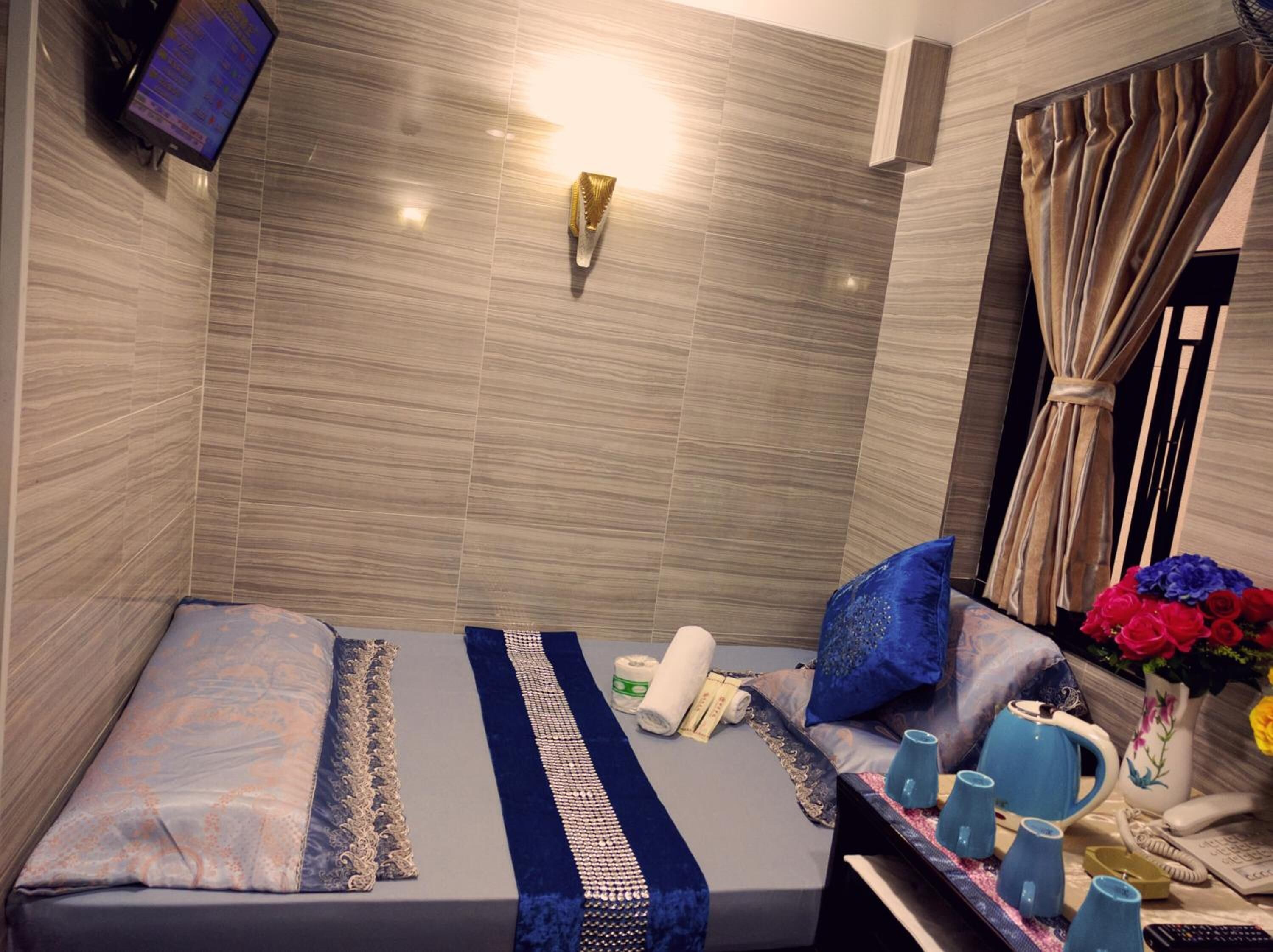Habitación de hotel con cama, televisor montado en la pared, mesita de noche con un florero y ventana con cortinas.