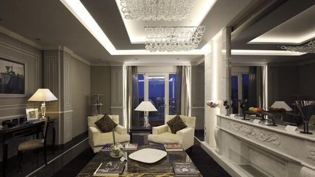 A luxurious hotel lobby with a marble coffee table, two sofas, a chandelier, and a city view through the glass doors. - Il Corso Suite (Rome)
