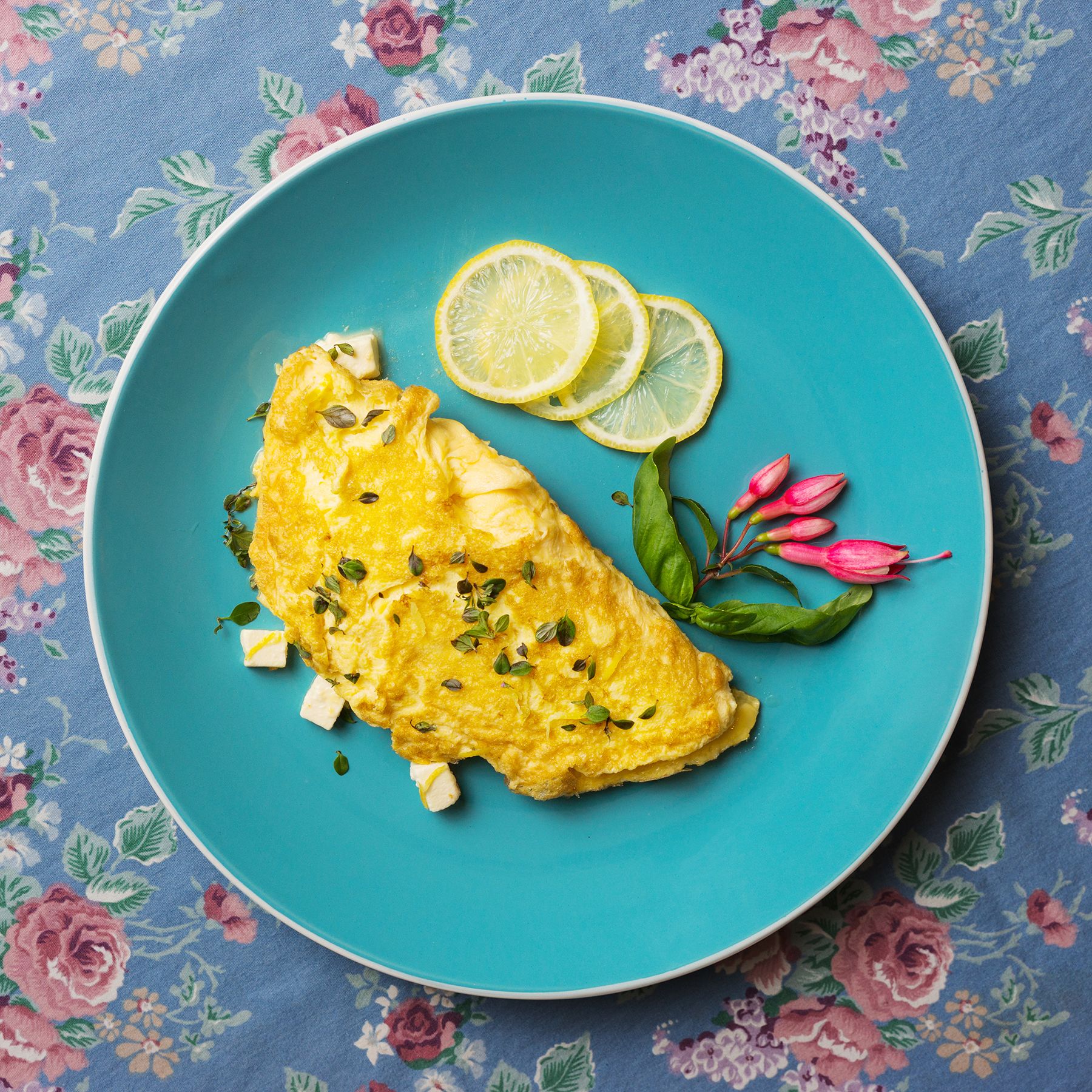 A plate with an omelette, lemon slices, and herbs.