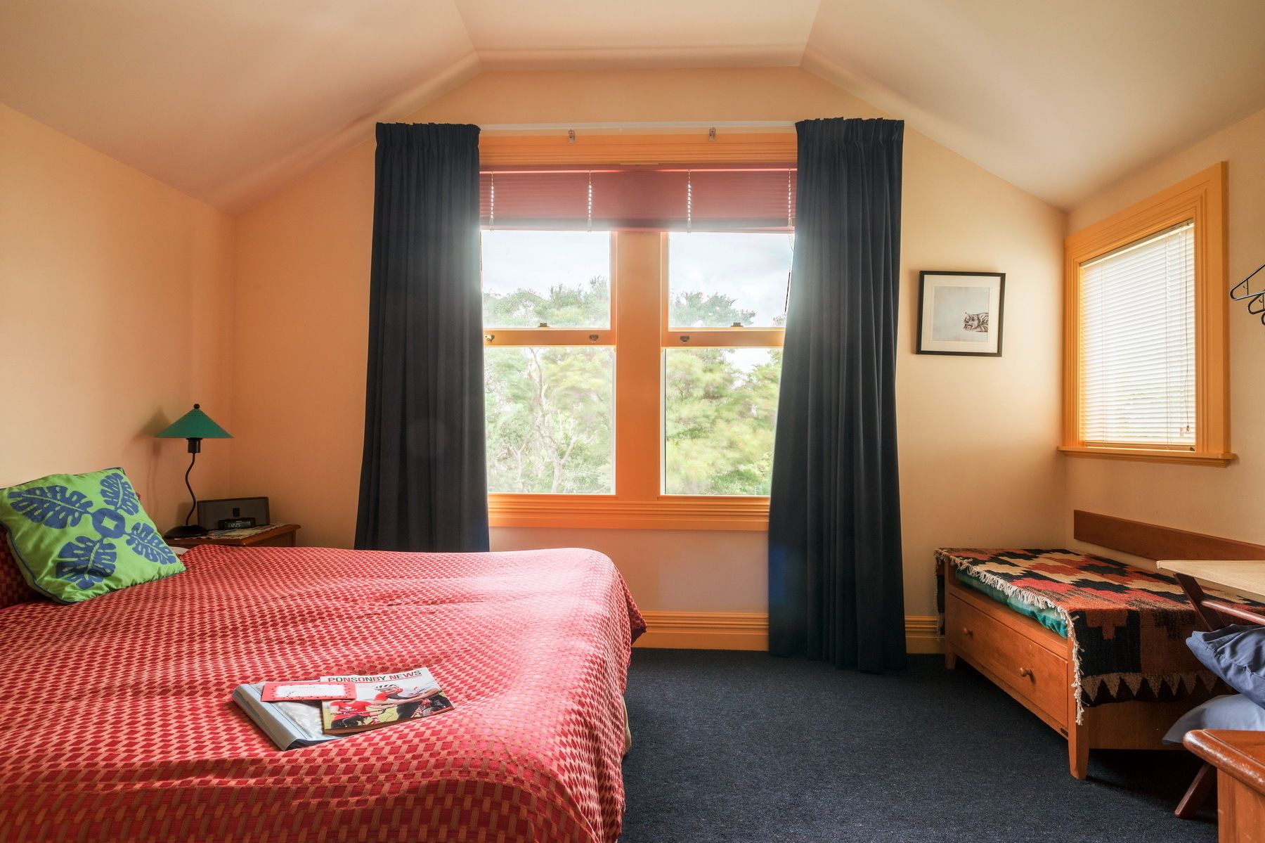 A bedroom with a bed, a small desk, a chair, a window with curtains, and a lamp.