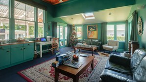 Un soggiorno con pareti color acquamarina, soffitto in legno, un albero di Natale, un divano in pelle e un tavolo da pranzo con libri e un computer portatile.