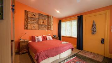 A bedroom with a bed, a nightstand, a wall tapestry, a window with curtains, and a door with a sign.