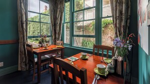 Zona pranzo con tavolo e sedie in legno, un vaso con fiori e vista sul verde circostante.