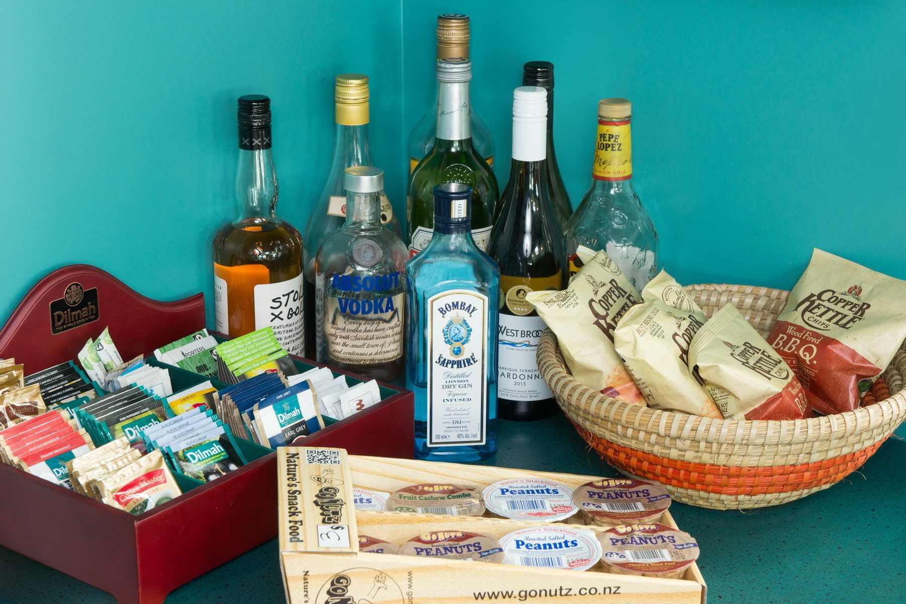Una selezione di snack, tra cui arachidi e patatine, una bottiglia di gin Bombay Sapphire, e diverse bottiglie di vodka e vino.