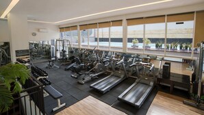 Un gimnasio amplio con diversos equipos de ejercicio, ventanas grandes y vistas a una piscina exterior.