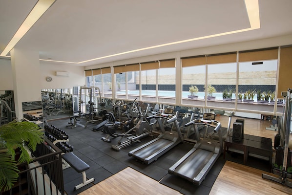 A spacious gym with various exercise equipment, large windows, and a view of a pool outside.
