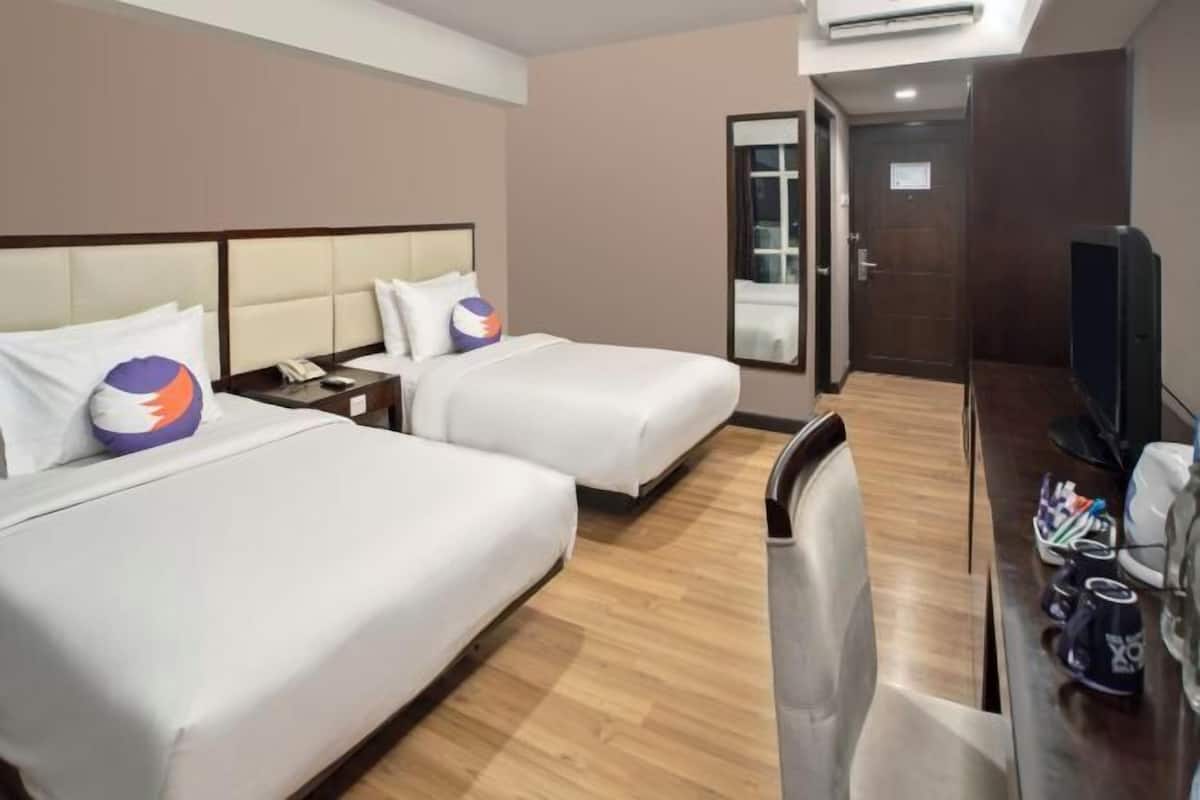 Ein Hotelzimmer mit zwei Betten, einem Schreibtisch mit Stuhl, einem Fernseher und einer Klimaanlage.