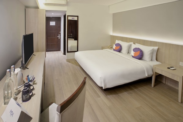 Une chambre d’hôtel avec un grand lit, des tables de chevet, un bureau avec une chaise, une télévision et un miroir.