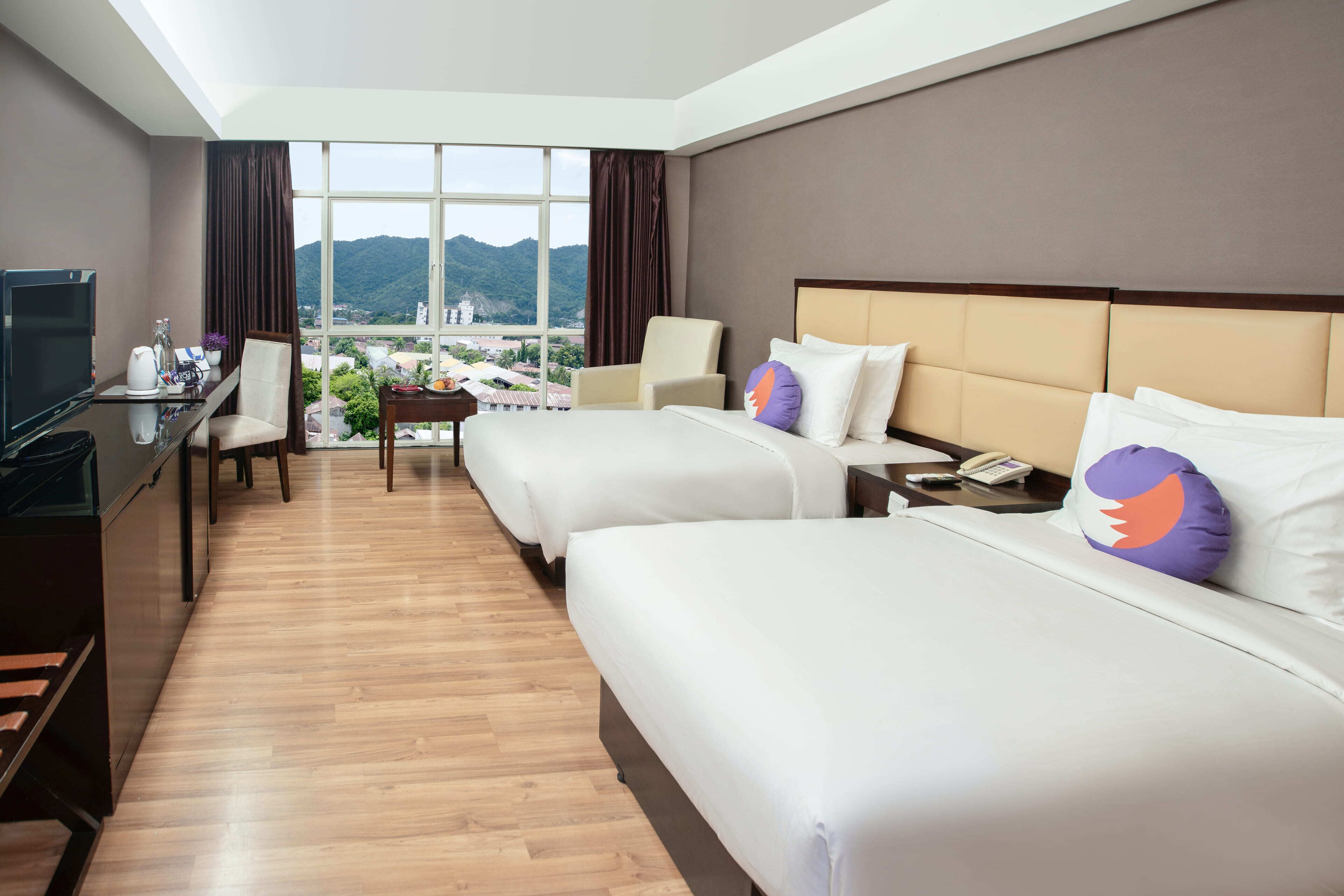 A hotel room with two beds, a desk with a TV, and a view of mountains.