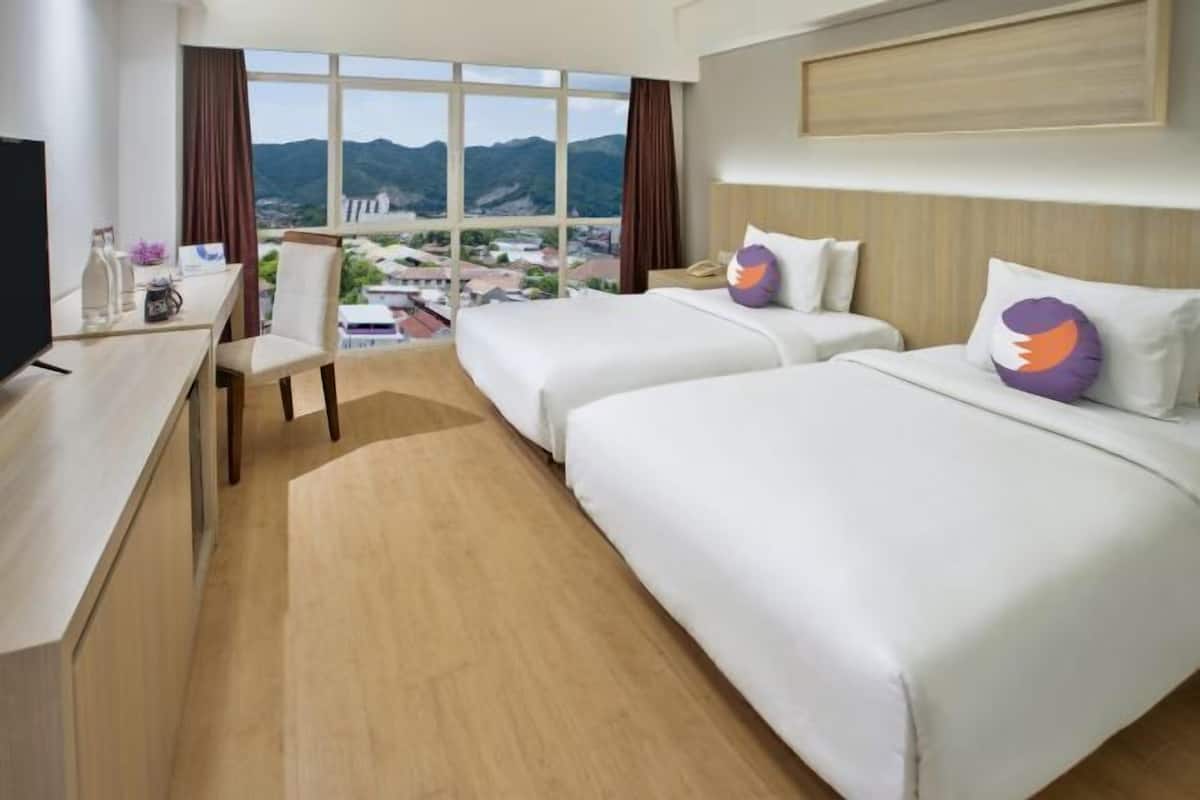 Ein Hotelzimmer mit zwei Betten, einem Schreibtisch, einem Stuhl, einem Fernseher und einem großen Fenster mit Blick auf die Berge.