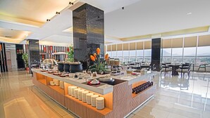 Un moderno vestíbulo de hotel con una zona de buffet central, amplias ventanas con vistas a la ciudad y un área de estar espaciosa.