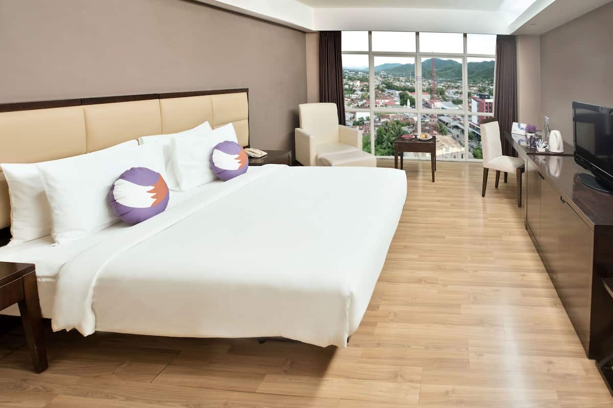 Ein Hotelzimmer mit einem großen Bett, einem Schreibtisch, einem Sessel, einem Fernseher und Blick auf die Stadt.