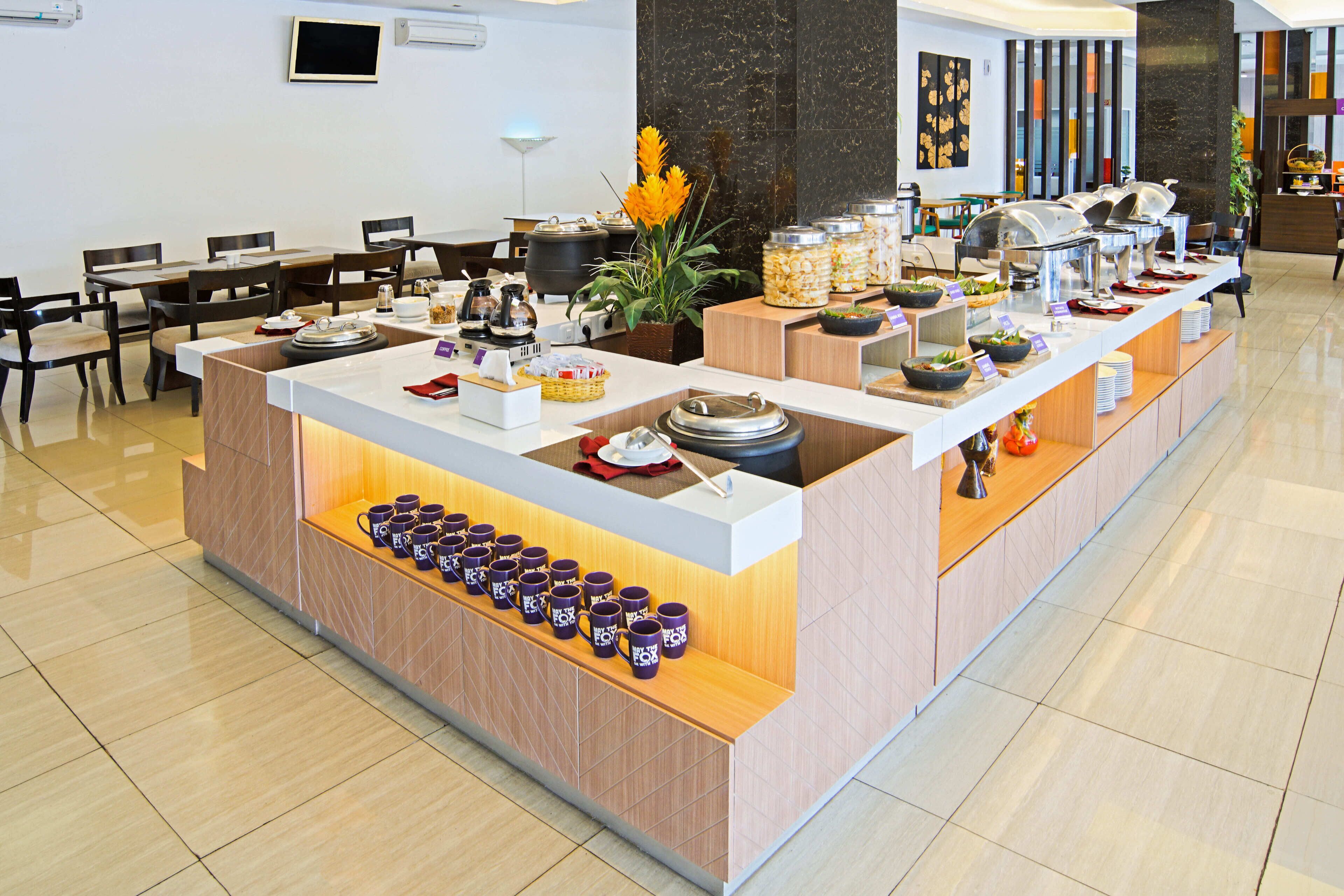 A buffet setup with various food items and utensils, a coffee station, and a seating area with tables and chairs.