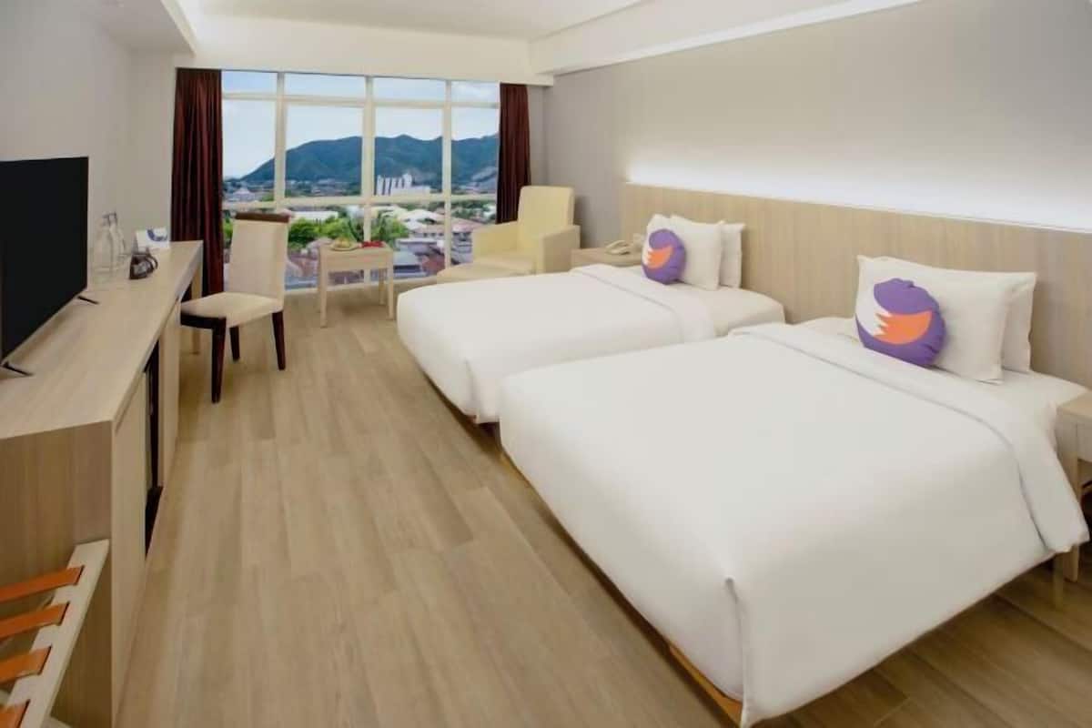 Ein Hotelzimmer mit zwei Betten, einem Schreibtisch mit Fernseher, einem Sessel und Blick auf die Stadt.
