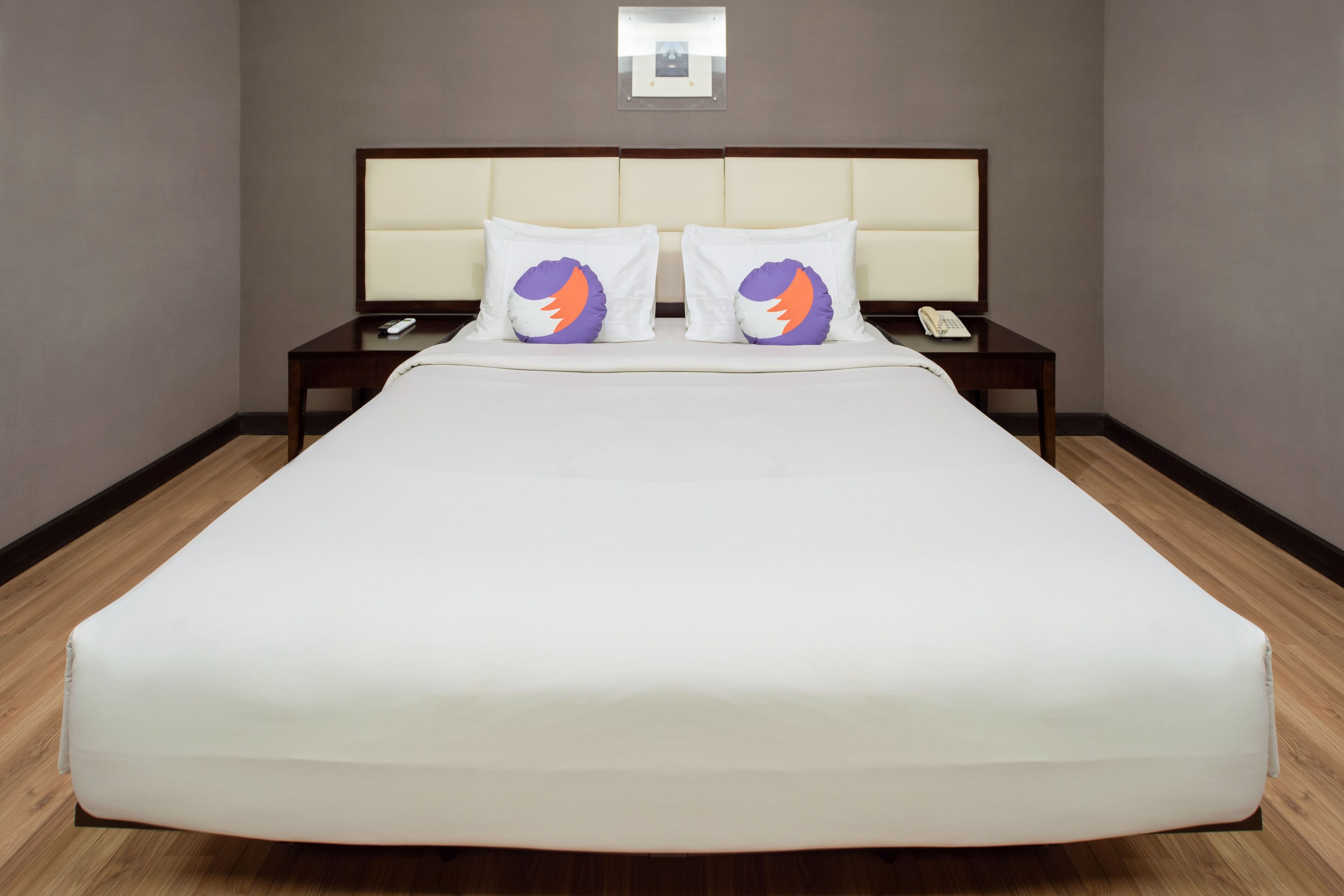 A hotel room with a large bed, two nightstands, a remote control, and a framed picture on the wall.