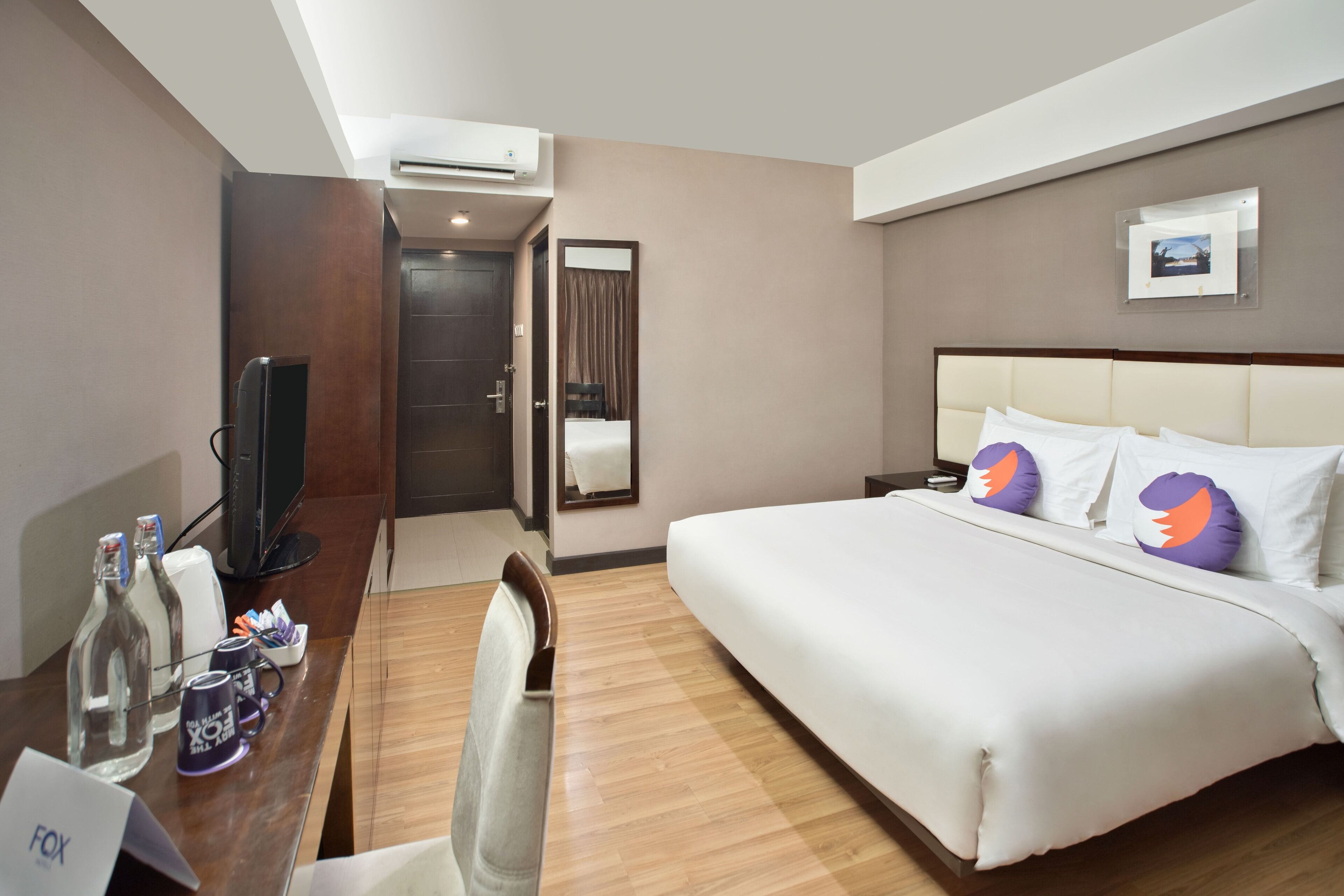 A hotel room with a bed, a desk with a computer, a chair, a TV, and a minibar.