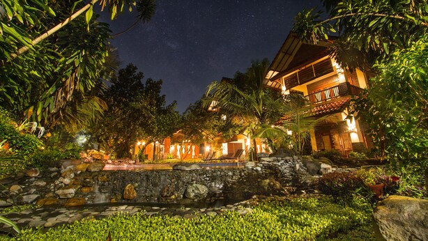 Un hotel con cascada de piedra, exuberante vegetación y cielo nocturno estrellado.