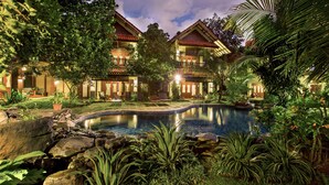 Un resort con piscina, abundante vegetación y un edificio bien iluminado con varios balcones.