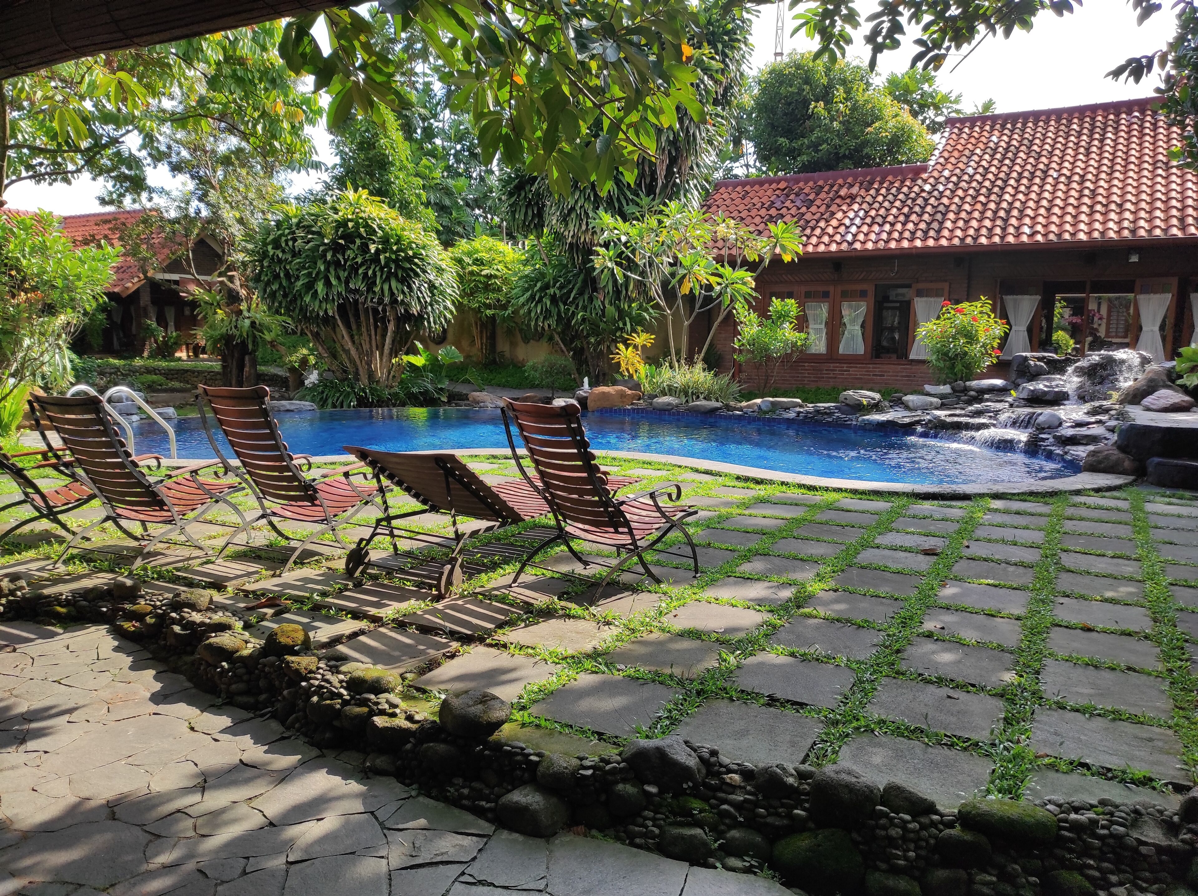 A pool area with lounge chairs, a stone pathway, and a small waterfall.