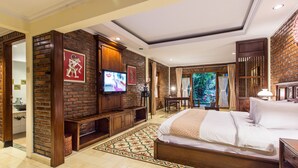 Habitación de hotel con pared de ladrillo, televisor, cama, escritorio y vista a zonas verdes.