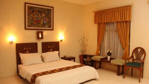 Habitación de hotel ordenada con una cama grande, lámparas de noche, una mesita con un florero y dos sillas.