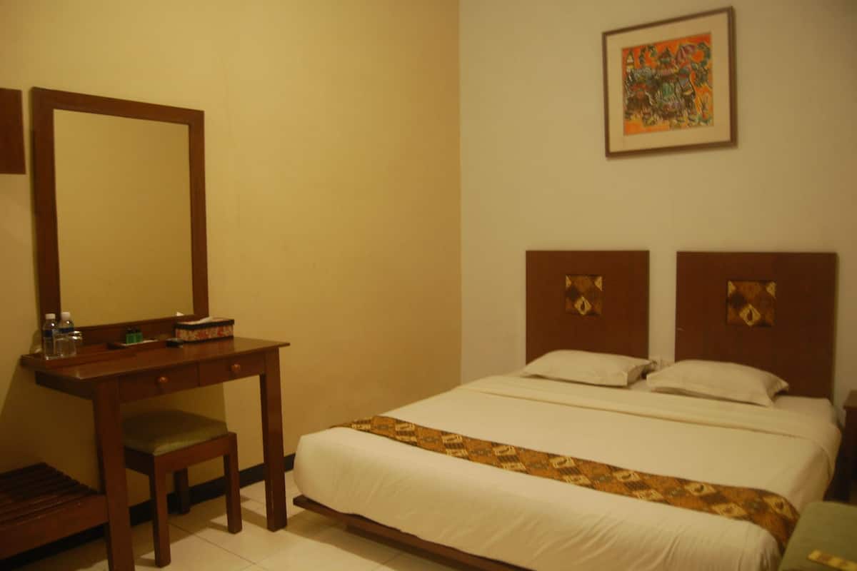 Habitación de hotel con cama, un escritorio de madera con silla, un espejo y un cuadro en la pared.