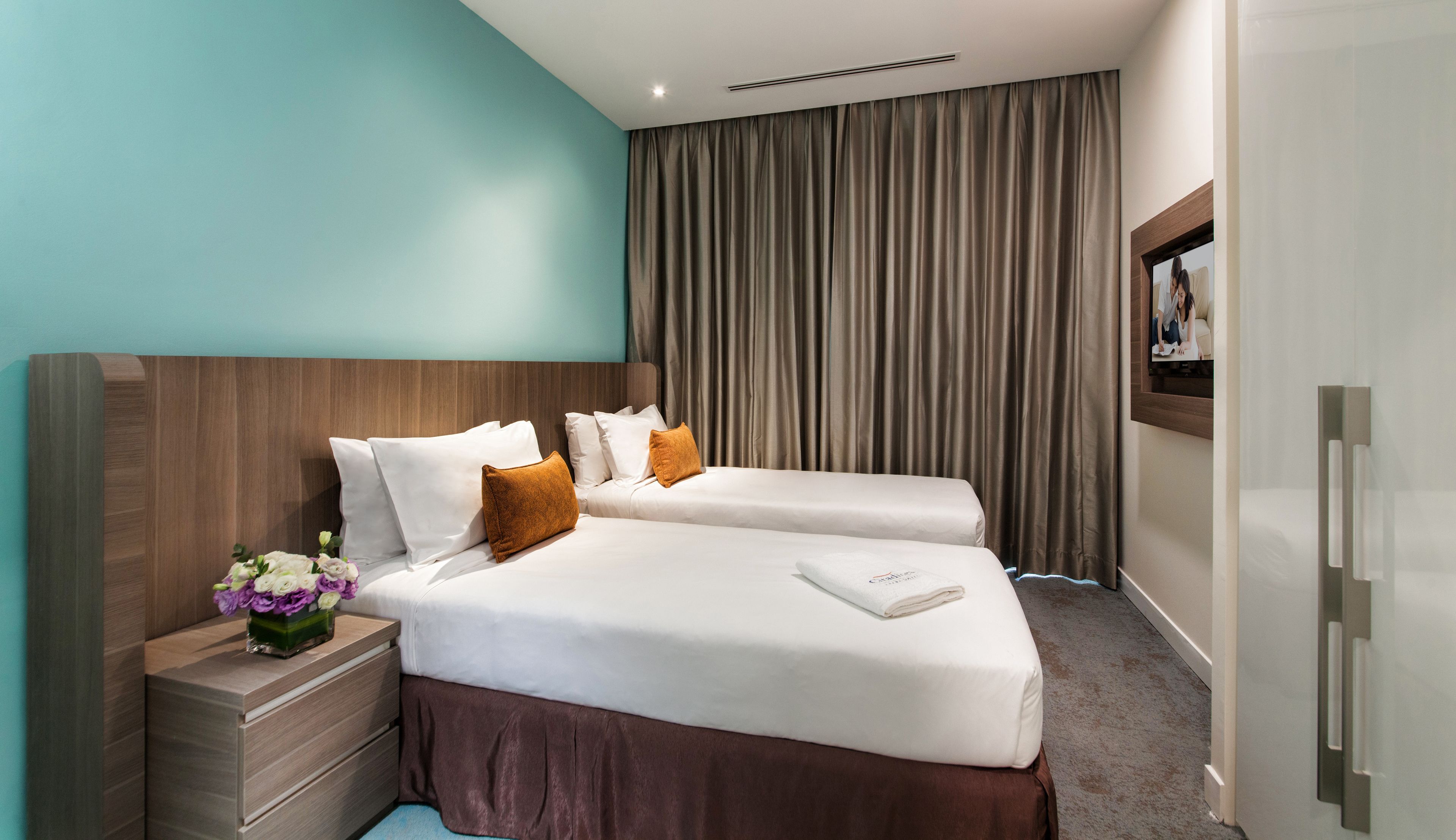 Een hotelkamer met een bed, nachtkastje, spiegel en raam met gordijnen.