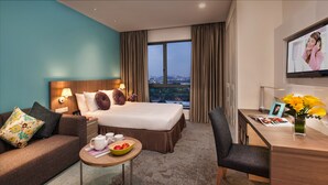A hotel room with a large bed, a desk, a chair, a small table with a bowl of fruit, and a TV on the wall. - Citadines DPulze Cyberjaya (Cyberjaya)